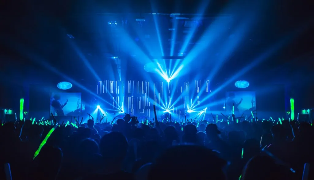 Silhouette in night club under blue rays beam and young people holding light saber enjoying at concert concept.