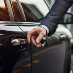 A businessman's hand reaches for the door of a luxury car. Background with selective focus